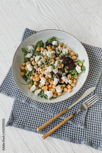 Salad of chickpeas, arugula, cheese, beets, cashews, pumpkin seeds with a dressing of olive oil, freshly ground pepper and salt. White background. Wooden table. Healthy food.
