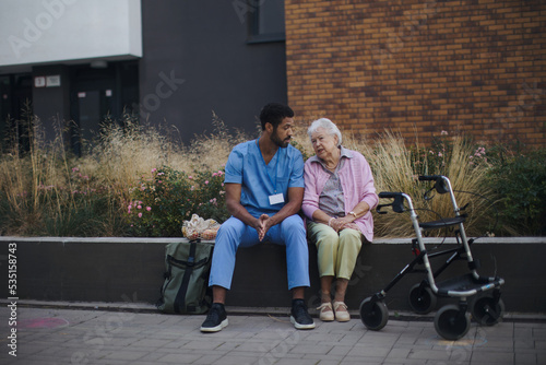 Happy senior woman sitting and talking with medical assistant in front of nurishing home. photo