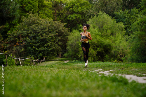 Young black woman smiling while running in summer park