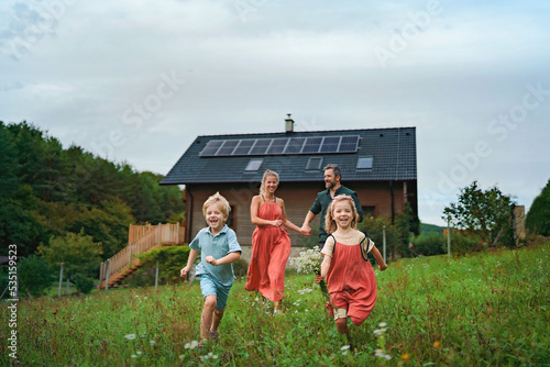 Happy family running near their house with solar panels. Alternative energy, saving resources and sustainable lifestyle concept. © Halfpoint