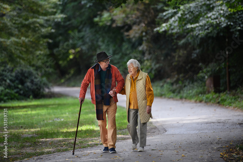 Happy senior couple in autumn clothes walking in city park together.