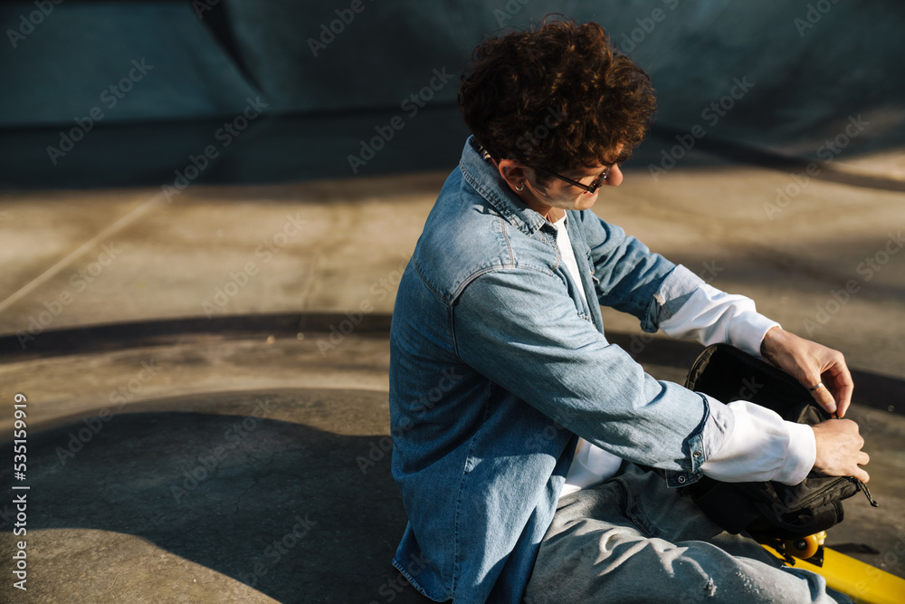 Young curly stylish boy in glasses closing his backpack