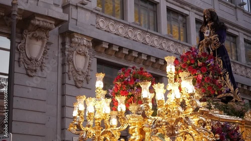 Close up of Jesus de Nazaret illuminated carriage during Good Friday on Holy Week procession, Madrid, Spain. Christ figure rocks as the bearers march.