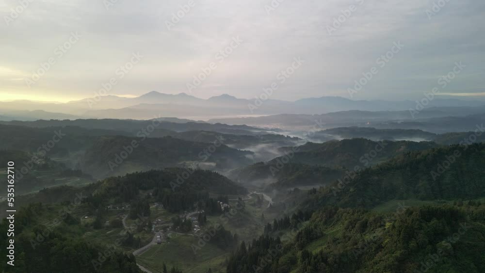 山々の谷間に雲海が現れる里山の夜明けをドローンで撮影