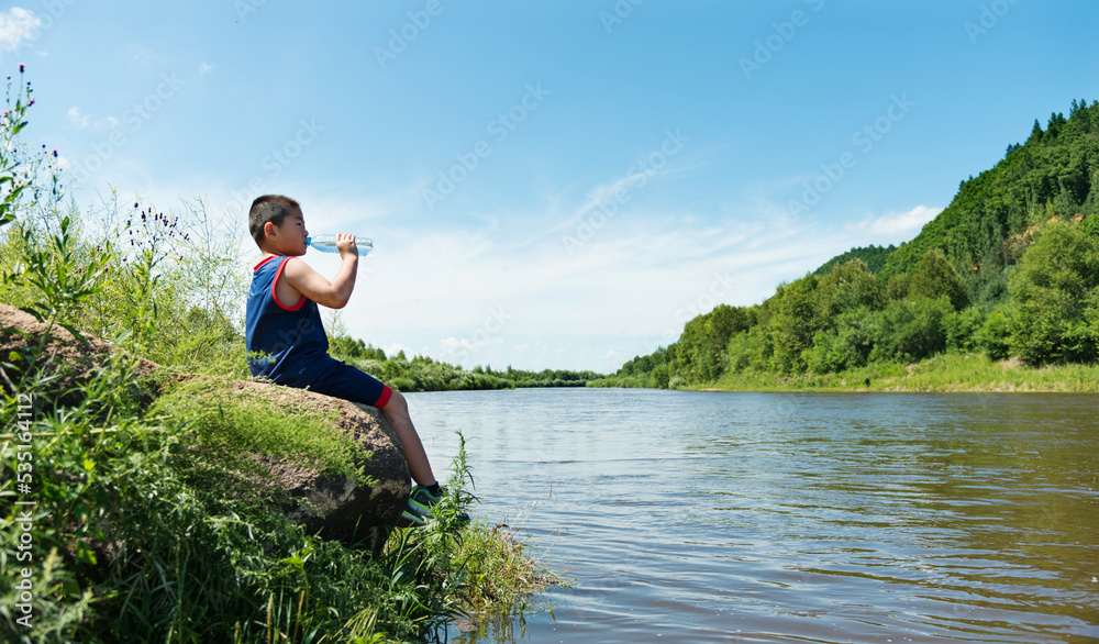 Naklejka premium Little asian boy drinking water by the lake