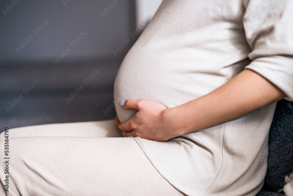 Pregnant woman relaxing at home. She is sitting on bed in bedroom.