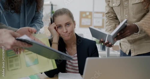 Portrait of exhausted young business lady sitting at desk while group of people are demanding work and attention in office. People and career concept.