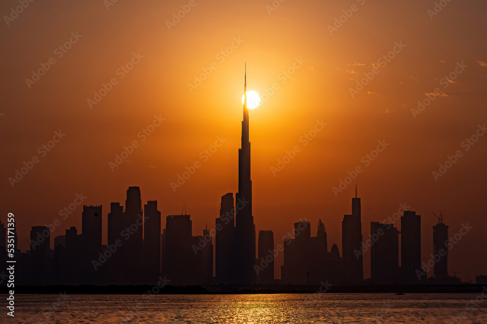 Oct 1st, 2022 - Dubai, UAE: Sun passing through the landscape of Dubai city skyline and Burj Khalifa silhouette
