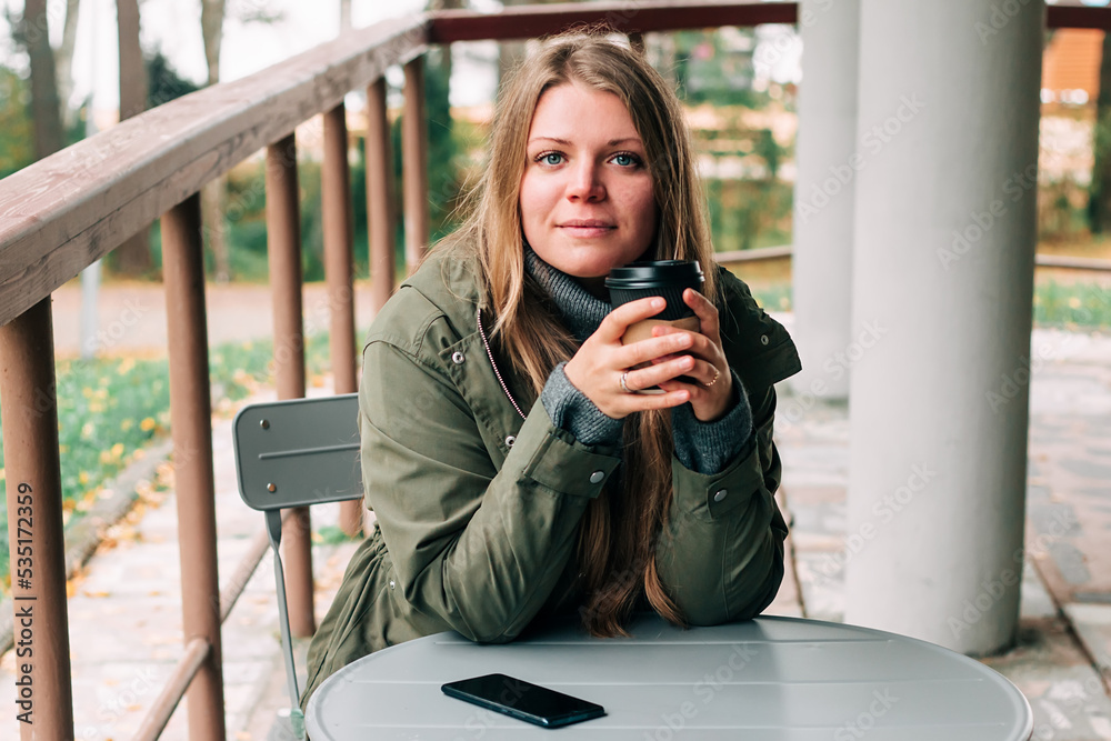 Young woman sitting on outdoor terrace in the forest drinking a cup of hot coffee. Beautiful female relax and enjoy outdoor activity lifestyle in nature on autumn travel vacation. Young woman sitting on outdoor terrace in the forest drinking a cup of hot coffee. Beautiful female relax and enjoy outdoor activity lifestyle in nature on autumn travel vacation.