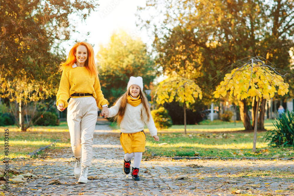 Fototapeta premium Happy mother and daughter walking in the park. Family enjoying the beautiful autumn nature.