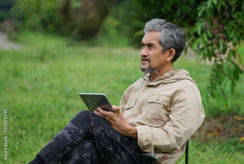 a senior man resting on camping chair, a male older adult thinking while using tablet computer in the garden,concept elderly people lifestyle, hobby, small business owner in farm, casual business