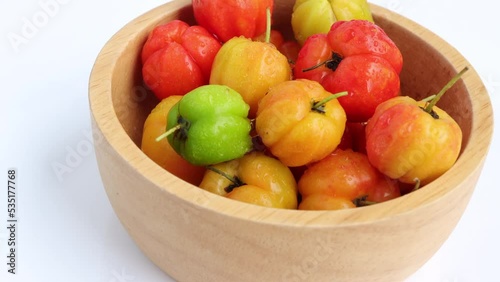 Barbados cherry, Malpighia emarginata, red acerola cherry in wooden bowl. Selective focus. Rotating on turn table.  photo