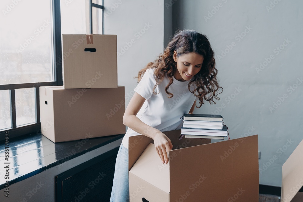 Happy woman packing carton box with things, relocating in new home. Moving, real estate rental Happy woman packing carton box with things, relocating in new home. Moving, real estate rental