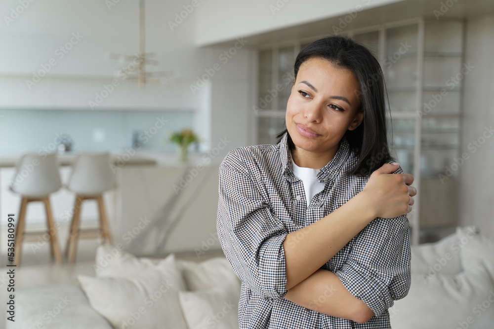 Calm happy female embraces herself feeling self love, self-pride, dreaming, standing at cozy home Calm happy female embraces herself feeling self love, self-pride, dreaming, standing at cozy home