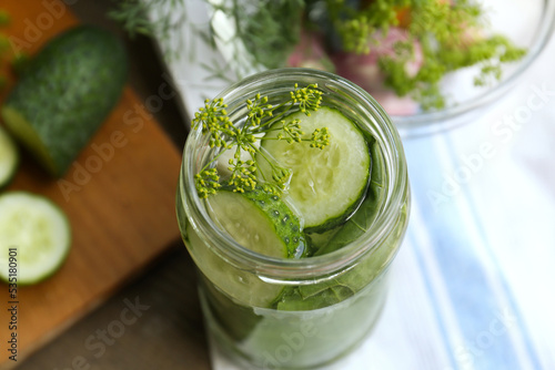 Glass jar with cucumber slices, dill and brine on table, closeup. Pickling recipe