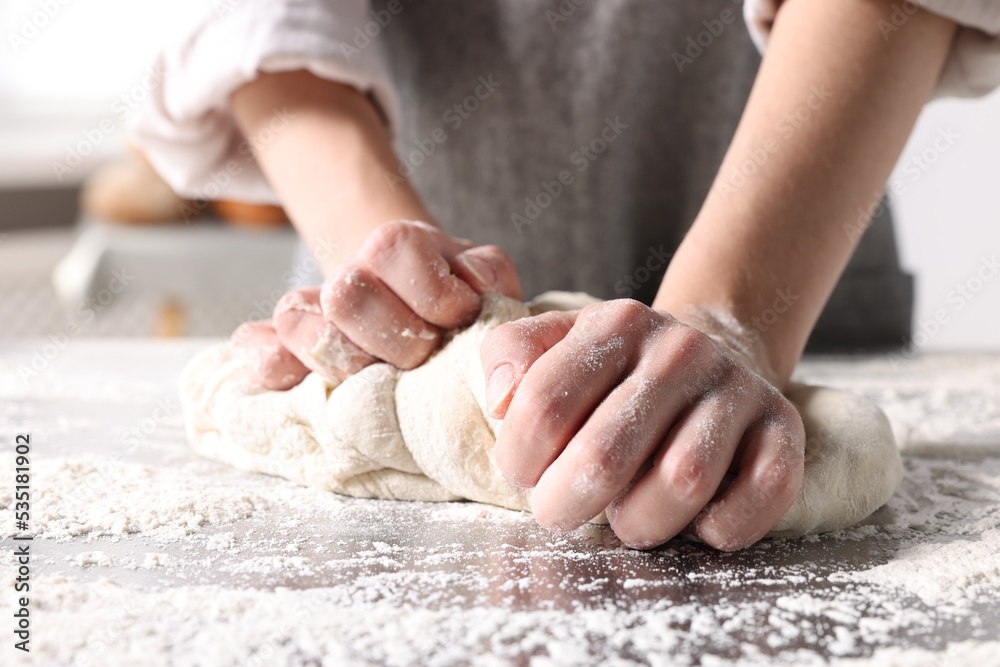 Woman kneading dough at table in kitchen, closeup