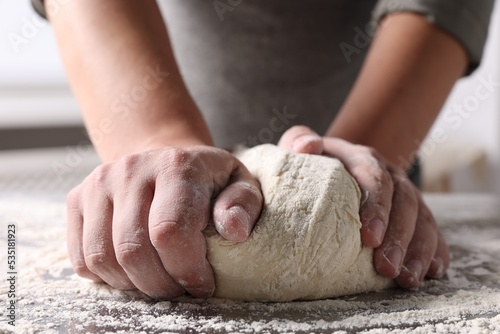 Man kneading dough at table in kitchen, closeup