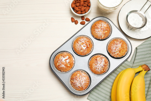 Flat lay composition with homemade banana muffins and milk on white wooden table. Space for text