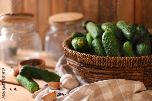 Fresh cucumbers and other ingredients near empty jars prepared for canning on wooden table, closeup
