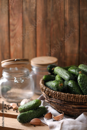 Fresh cucumbers and other ingredients near empty jars prepared for canning on wooden table