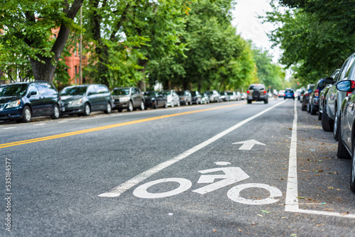 carril bici con señal pintada en el asfalto de la calle y con coches aparcados y coche de fondo photo