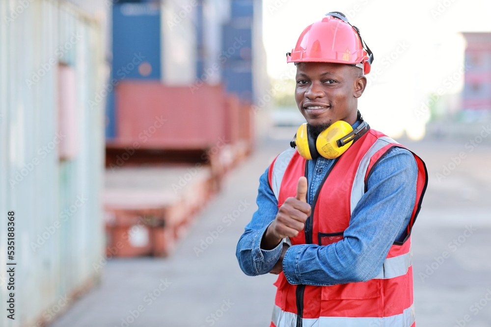 Foreman engineer standing and crossed arms while showing thumb up with happy and success face. Confident engineering work at container cargo site and checking industrial container cargo freight ship Foreman engineer standing and crossed arms while showing thumb up with happy and success face. Confident engineering work at container cargo site and checking industrial container cargo freight ship