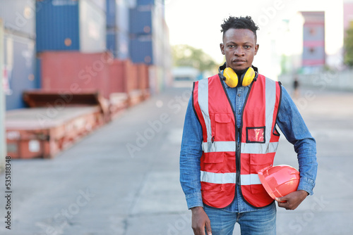 Foreman engineer standing and crossed arms while looking at camera with happy and success face. Confident engineering work at container cargo site and checking industrial container cargo freight ship