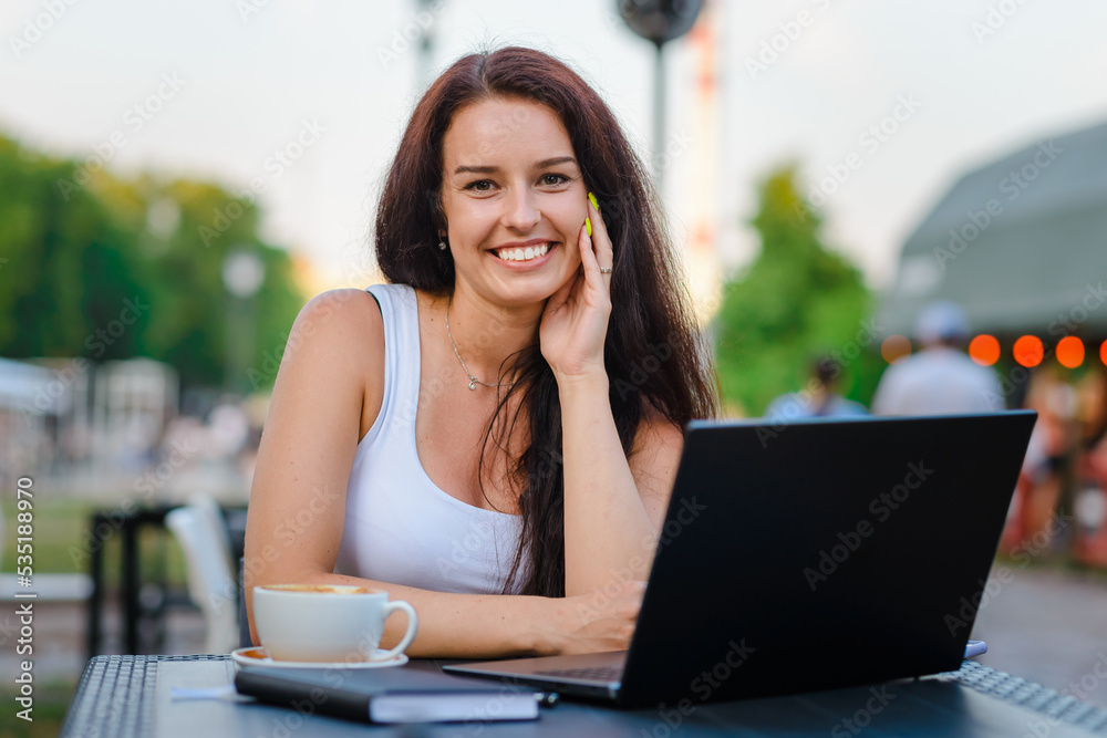 Smiling sensuality caucasian business woman with brunette hair working on laptop in outdoor cafe. College student using technology ,online education, freelance.Summer day.