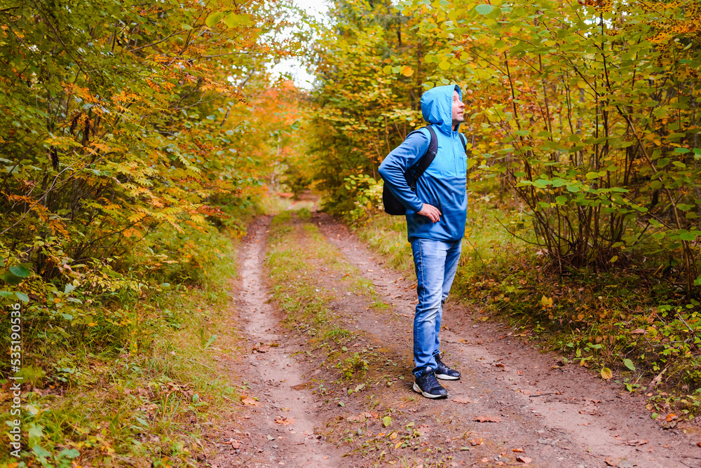 Fototapeta premium A middle age male hiker with a hoodie and backpack.Man standing along the autumn forest path way.A healthy lifestyle in nature.