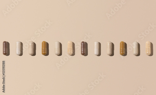 Mix of medical capsules in a line on light beige top view, hard shadows. Dietary supplements photo