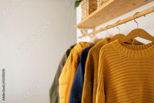 Autumn knitted sweaters hang on wooden hangers in the room