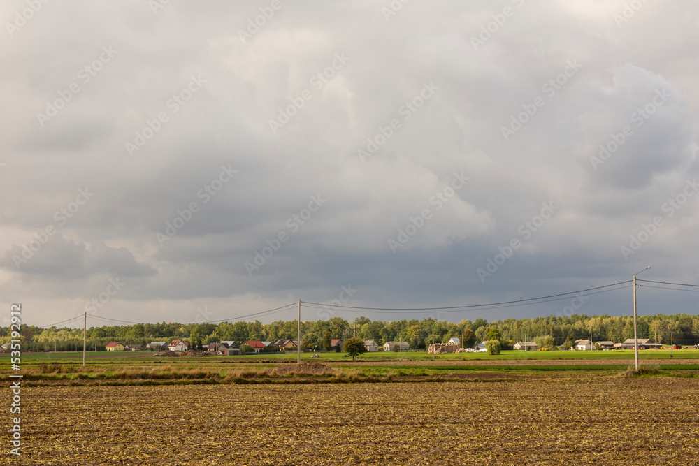 Dark clouds over the plowed field and the village in the background. Autumn.