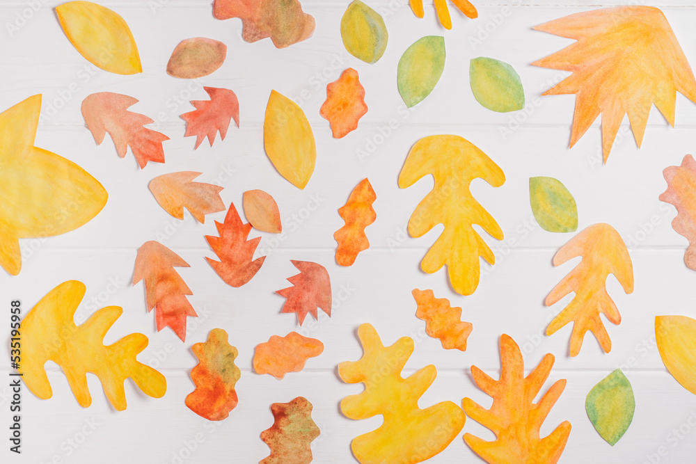 Background image of cut paper red, orange and yellow autumn leaves painted in watercolor laid out on white wooden planks. top view. DIY handmade autumn decorations Background image of cut paper red, orange and yellow autumn leaves painted in watercolor laid out on white wooden planks. top view. DIY handmade autumn decorations