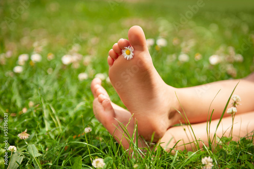 Child with chamomile between toes sitting on green grass outdoors, closeup of feet © New Africa