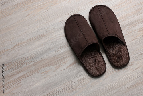 Pair of brown slippers on white wooden floor, top view. Space for text