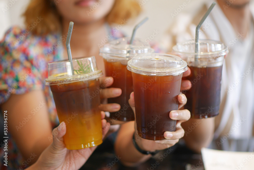 Iced Americano Black Coffee holding hand with friends (people) in take away cup (plastic glass) on the table in cafe. Iced Americano Black Coffee holding hand with friends (people) in take away cup (plastic glass) on the table in cafe.
