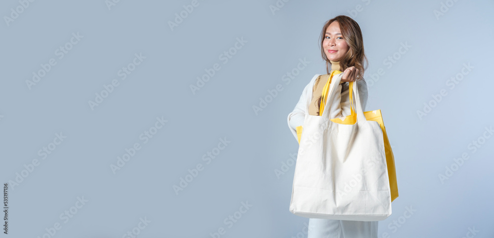 Panoramic shot of stylish young woman holding canvas tote bag standing on white background with empty space for your text. Panoramic shot of stylish young woman holding canvas tote bag standing on white background with empty space for your text.