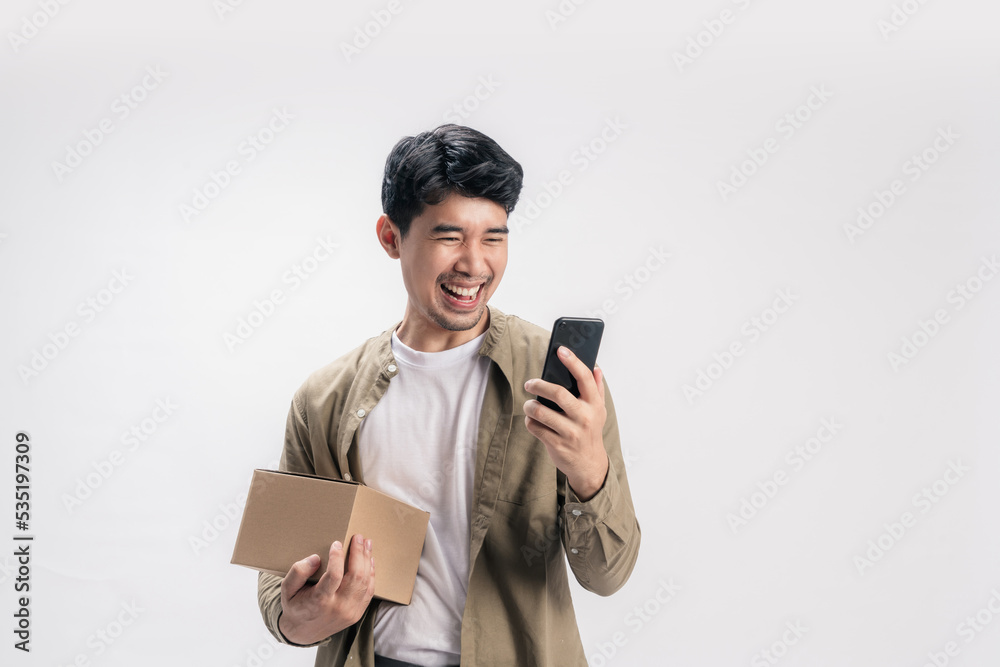 Portrait handsome Asian man in casual outfit, with holding a box and happy using online shopping on smartphone, with an exciting smile on isolated white background.