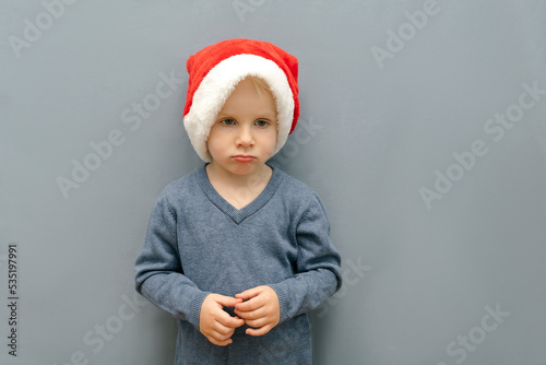Unhappy gloomy sad child kid boy in christmas red santa claus hat cap,New Year. Christmas Holidays.