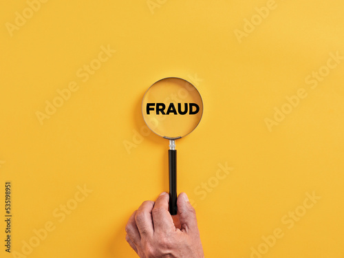 Male hand holds a magnifier focusing on the word fraud. To search, find, discover or reveal a fraud attempt