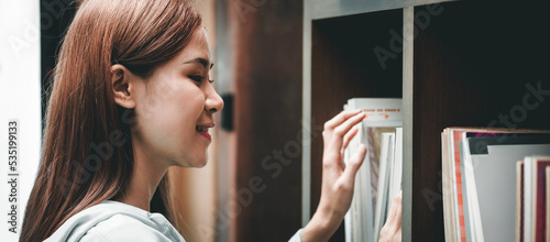Εκτύπωση καμβά Female student is standing in front of the bookshelf to choosing textbook or lit