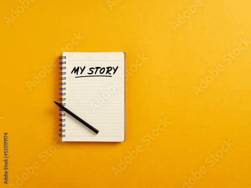 Notepad and black pen on yellow background with the handwritten word my story. Telling about yourself and biography photo