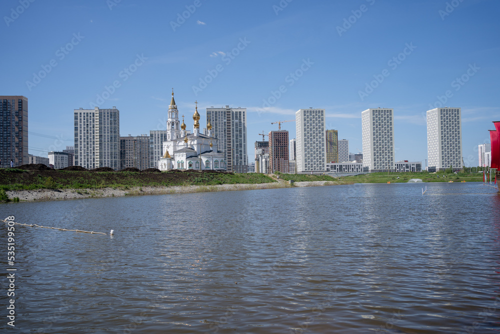 The Russian Orthodox Church stands on the banks of the river against the backdrop of modern houses. High quality photo