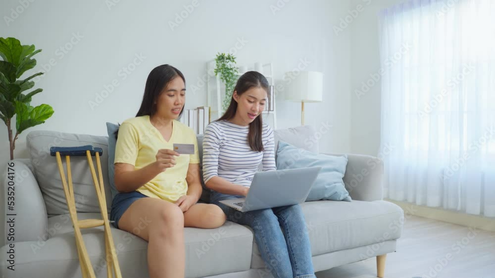 Asian woman amputee using laptop computer with friend in living room. Asian woman amputee using laptop computer with friend in living room.
