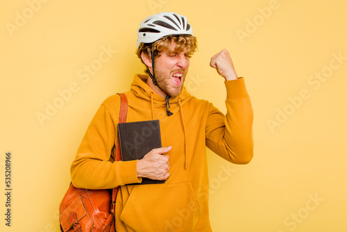 Young student man wearing a helmet bike isolated on yellow background raising fist after a victory, winner concept.