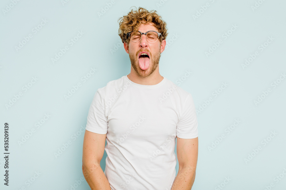 Young caucasian man isolated on blue background funny and friendly sticking out tongue. Young caucasian man isolated on blue background funny and friendly sticking out tongue.