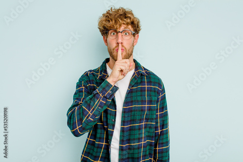 Photography Young caucasian man isolated on blue background keeping a secret or asking for silence