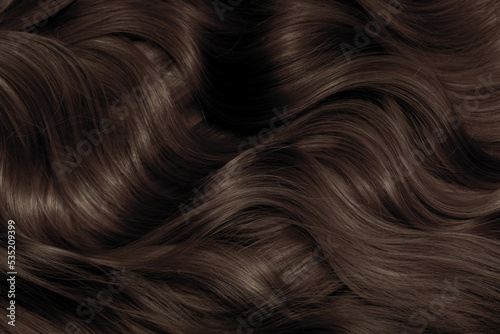 Brown hair close-up as a background. Women's long brown hair. Beautifully styled wavy shiny curls. Hair coloring. Hairdressing procedures, extension. © Vera