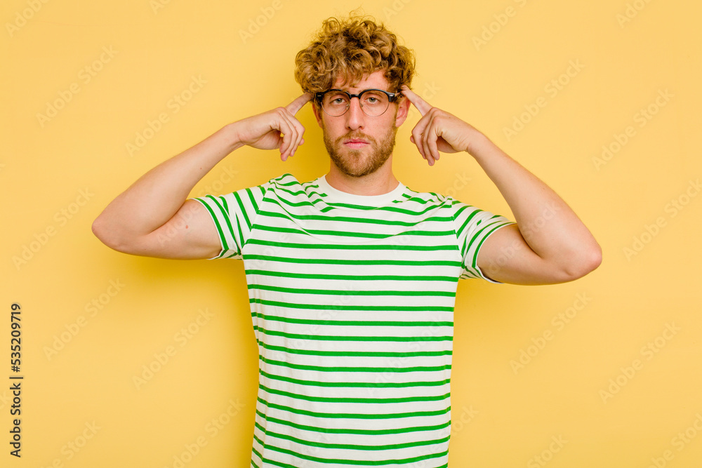 Young caucasian man isolated on yellow background focused on a task, keeping forefingers pointing head. Young caucasian man isolated on yellow background focused on a task, keeping forefingers pointing head.