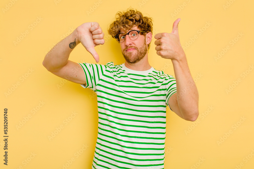 Young caucasian man isolated on yellow background showing thumbs up and thumbs down, difficult choose concept Young caucasian man isolated on yellow background showing thumbs up and thumbs down, difficult choose concept